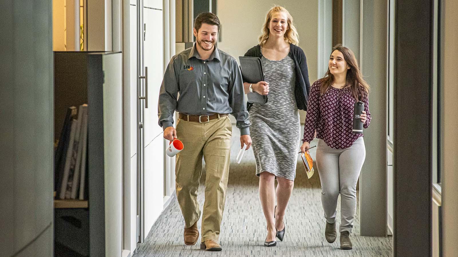 Three smiling alumni walking down a hallway at business